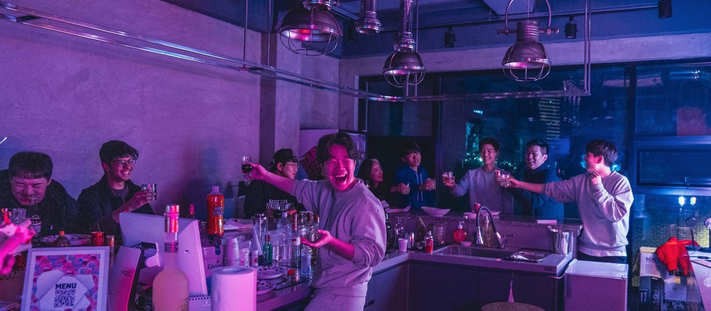 보랏빛 조명 아래 주방 바에서 건배하는 멤버들